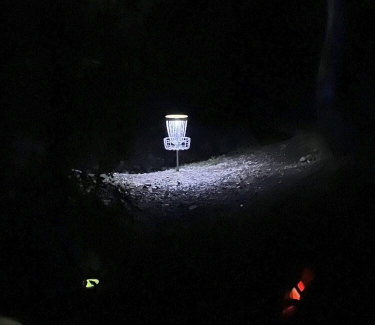 A disc golf basket at night that is lit up with a light.