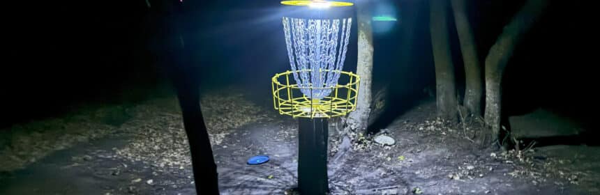 A disc golf basket lit up for a night round